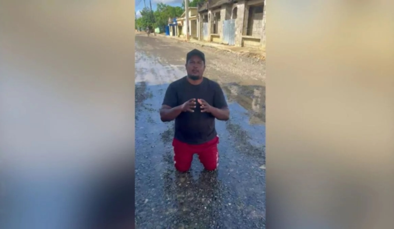 Regidor del PRM Manoli Montero de rodillas en una calle sin asfaltar de Pimentel, provincia Duarte, solicitando ayuda al presidente Luis Abinader.