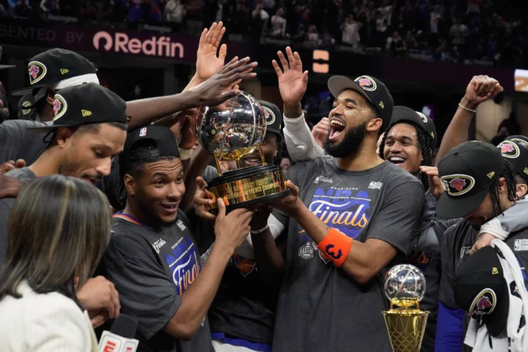 El pívot dominicano Karl-Anthony Towns sonríe eufórico junto a Jalen Brunson y sus compañeros de los Knicks de Nueva York mientras levantan el trofeo de campeones de la Conferencia Este en el tabloncillo.