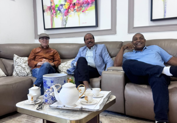 Los exalcaldes Manuel Jiménez con gorra, José Montás en el centro con chaqueta azul, y José Andújar a la derecha sonriendo en un sofá durante una reunión privada en una residencia.