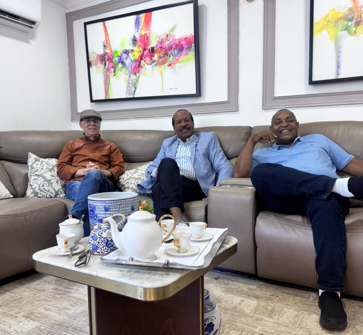 Los exalcaldes Manuel Jiménez con gorra, José Montás en el centro con chaqueta azul, y José Andújar a la derecha sonriendo en un sofá durante una reunión privada en una residencia.