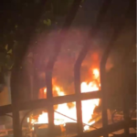 Llamaradas intensas provocadas por la quema de neumáticos en la avenida Independencia de Pimentel durante la noche, captadas a través de las rejas de hierro de una vivienda.