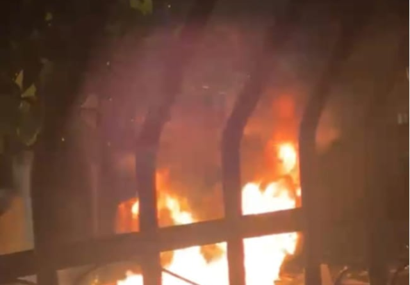 Llamaradas intensas provocadas por la quema de neumáticos en la avenida Independencia de Pimentel durante la noche, captadas a través de las rejas de hierro de una vivienda.