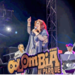 La maestra Belkys Concepción cantando con micrófono en mano sobre el gran escenario del festival Colombia al Parque en Bogotá, luciendo un elegante atuendo negro con detalles brillantes en las mangas y una sonrisa radiante ante el público.