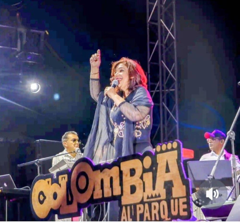 La maestra Belkys Concepción cantando con micrófono en mano sobre el gran escenario del festival Colombia al Parque en Bogotá, luciendo un elegante atuendo negro con detalles brillantes en las mangas y una sonrisa radiante ante el público.