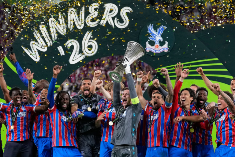El delantero Jean-Philippe Mateta junto a sus compañeros del Crystal Palace levantando el trofeo de campeones de la UEFA Conference League en el podio de Leipzig, rodeados de confeti y celebrando de manera eufórica.