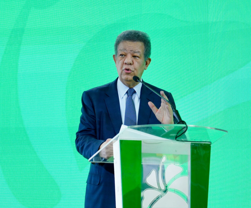 El líder político Leonel Fernández gesticula frente a un podio al lado de una pantalla digital que muestra gráficos de la deuda pública dominicana del año 2020 al 2026