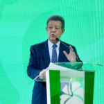 El líder político Leonel Fernández gesticula frente a un podio al lado de una pantalla digital que muestra gráficos de la deuda pública dominicana del año 2020 al 2026