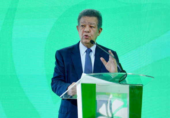 El líder político Leonel Fernández gesticula frente a un podio al lado de una pantalla digital que muestra gráficos de la deuda pública dominicana del año 2020 al 2026