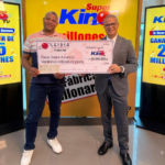 El director de sorteos de LEIDSA, Manuel Abreu, entrega un cheque certificado de veinticinco millones de pesos al camionero Óscar Beltré Amancio, ganador del Súper Kino TV en un set de televisión con fondo amarillo.