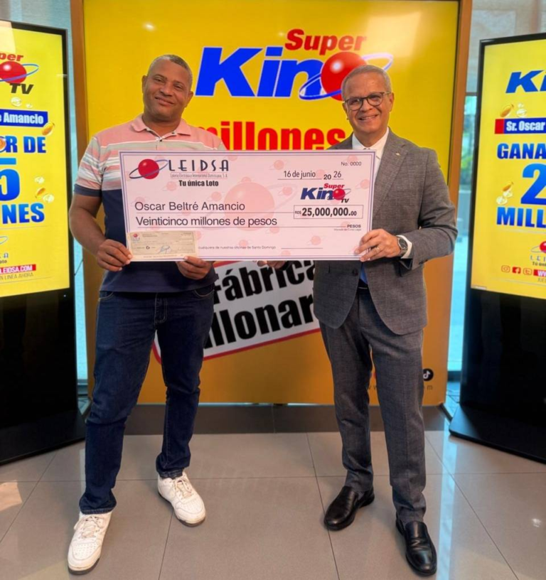 El director de sorteos de LEIDSA, Manuel Abreu, entrega un cheque certificado de veinticinco millones de pesos al camionero Óscar Beltré Amancio, ganador del Súper Kino TV en un set de televisión con fondo amarillo.