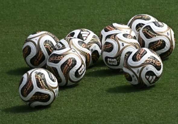 Primer plano de varios balones Trionda Final de color negro con detalles dorados y rosados sobre el césped del estadio Cotton Bowl de Dallas durante un entrenamiento.