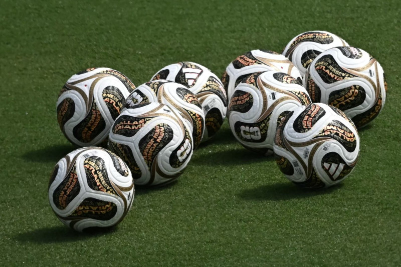 Primer plano de varios balones Trionda Final de color negro con detalles dorados y rosados sobre el césped del estadio Cotton Bowl de Dallas durante un entrenamiento.