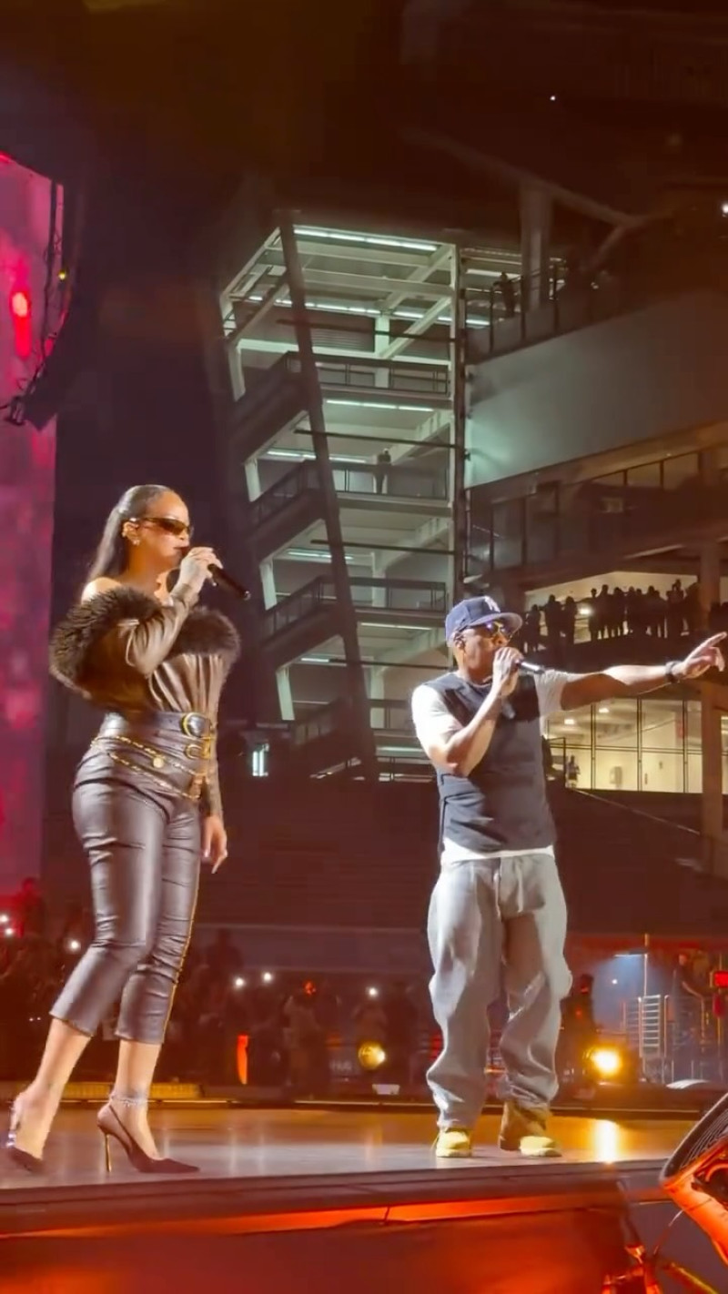 La cantante barbadense Rihanna cantando con un micrófono junto al rapero Jay-Z sobre el escenario iluminado del Yankee Stadium en Nueva York.